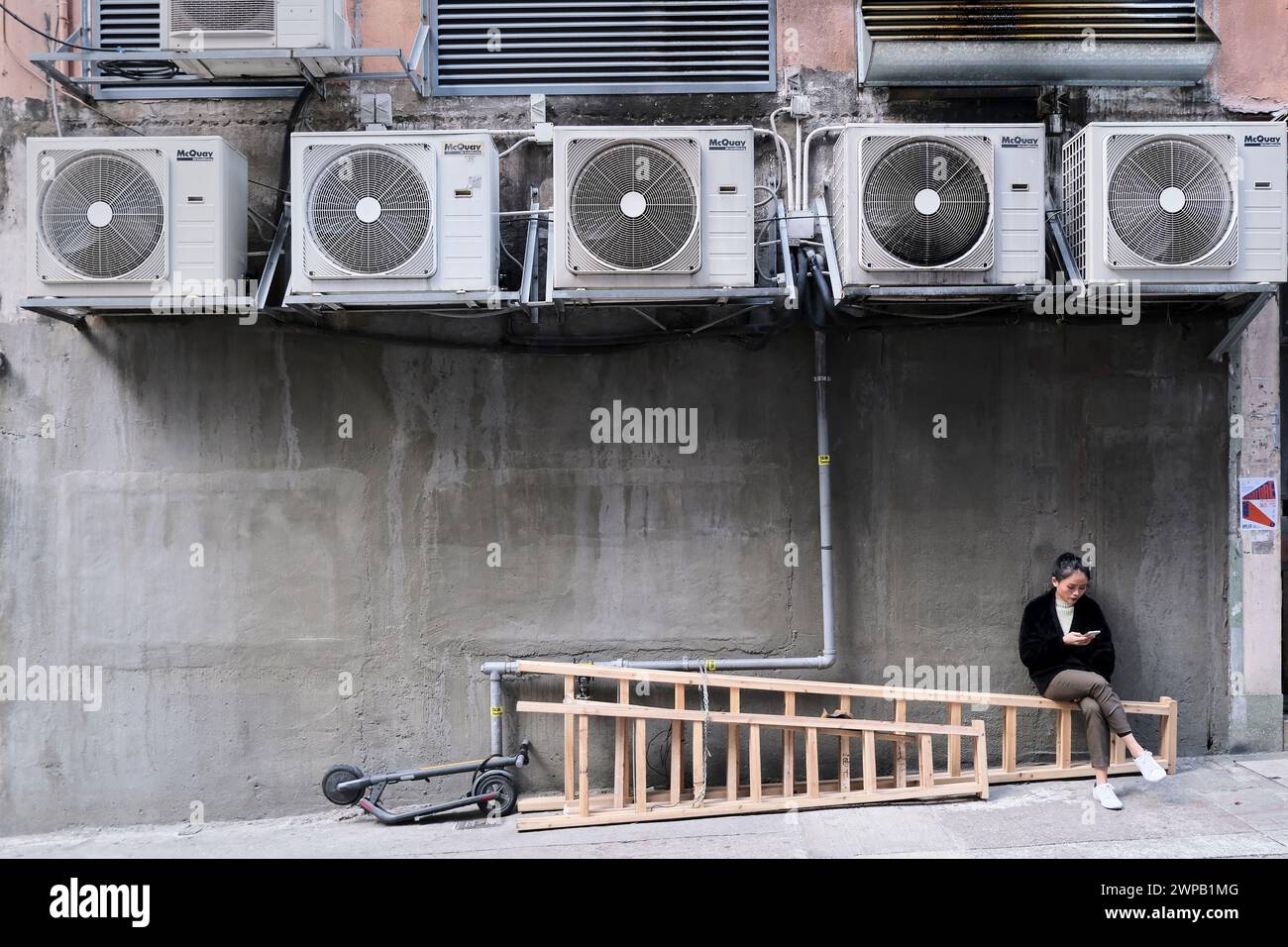 A woman takes a rest on a ladder under a row of air conditioning units. Stock Photo