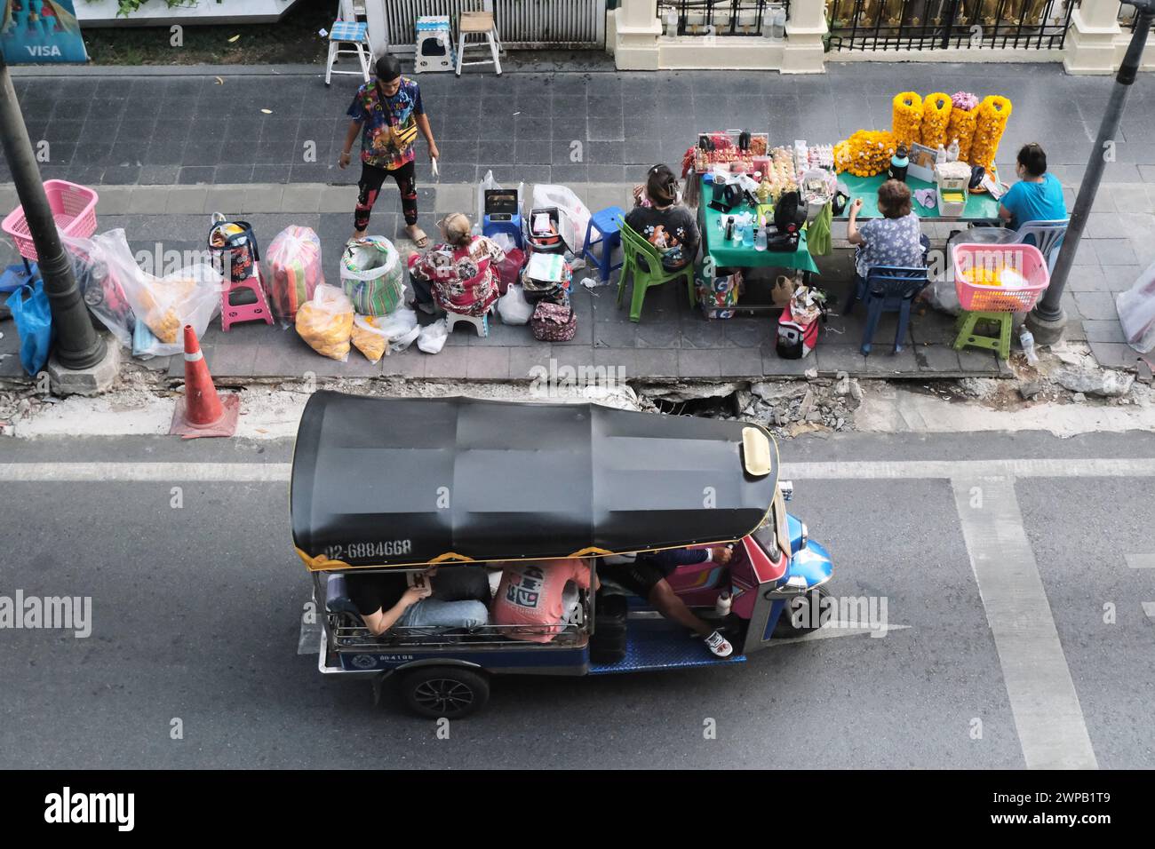 Bangkok, Thailand - February 20th 2024: A Tuk-Tuk passes street venders on a Bangkok pavement. Stock Photo