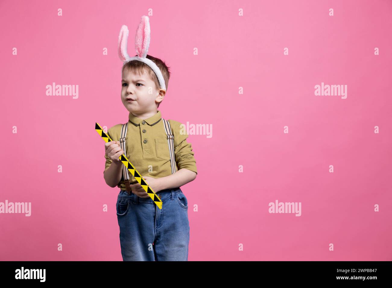 Upset little toddler playing with a toy and being displeased about something, wearing a pair of bunny ears for easter celebration. Young child feeling irritated and sad, adorable innocent kid. Stock Photo