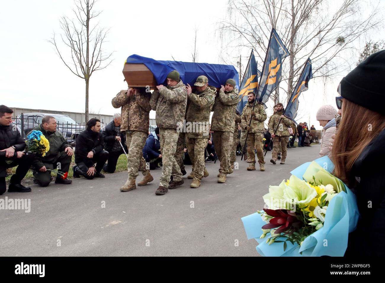 Non Exclusive: BUCHA, UKRAINE - MARCH 5, 2024 - Servicemen carry the coffin to the Alley of Heroes as members of the public kneel to show their respec Stock Photo