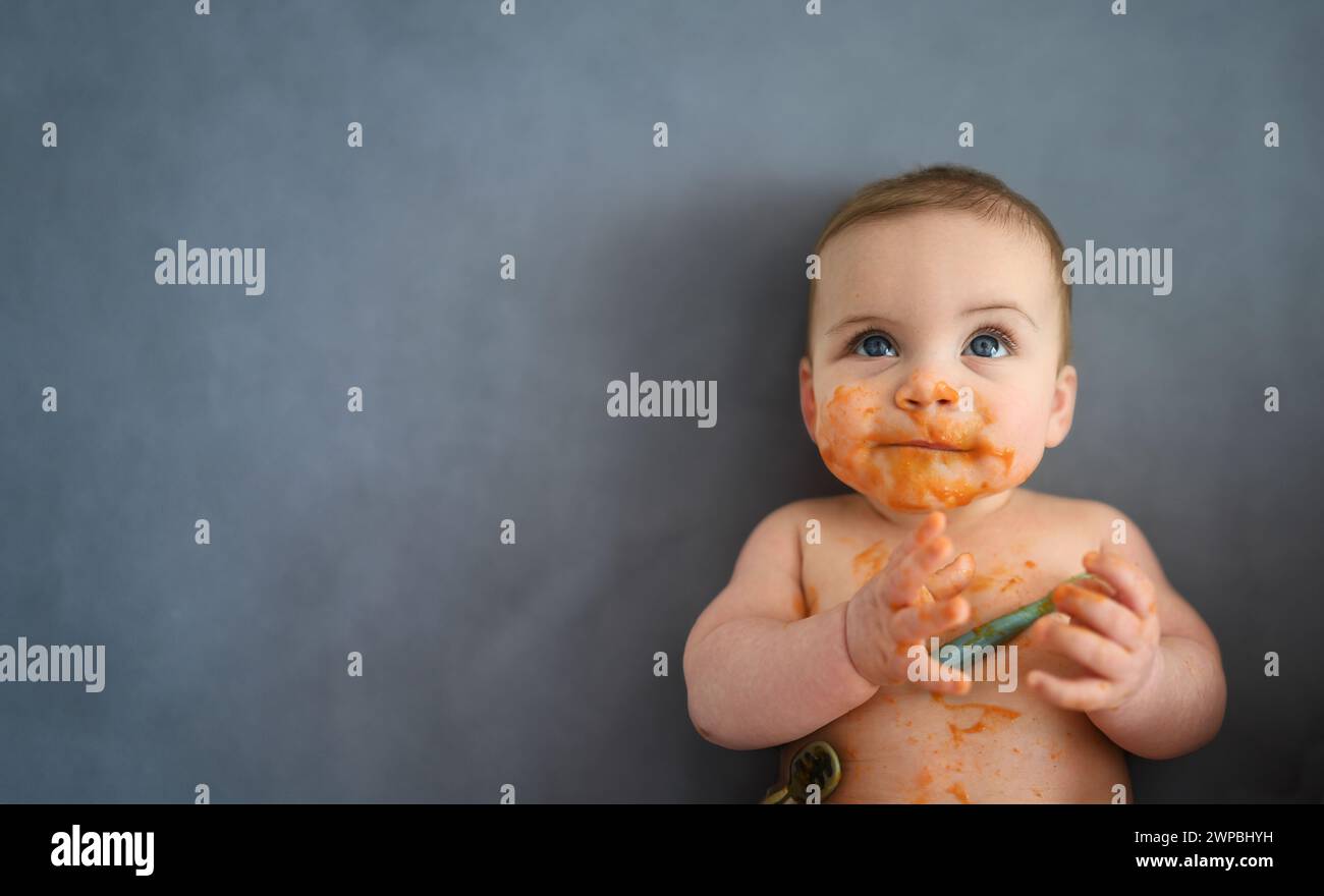 Cute adorable infant funny dirty baby trying to eat himself with fruit