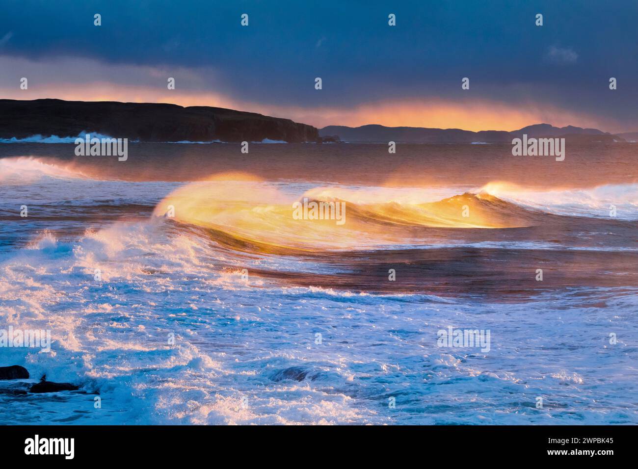 Big waves breaking in a winter storm, swirling spray illuminated by the warm light of the evening sun, Summer Isles in the background, United Kingdom, Stock Photo