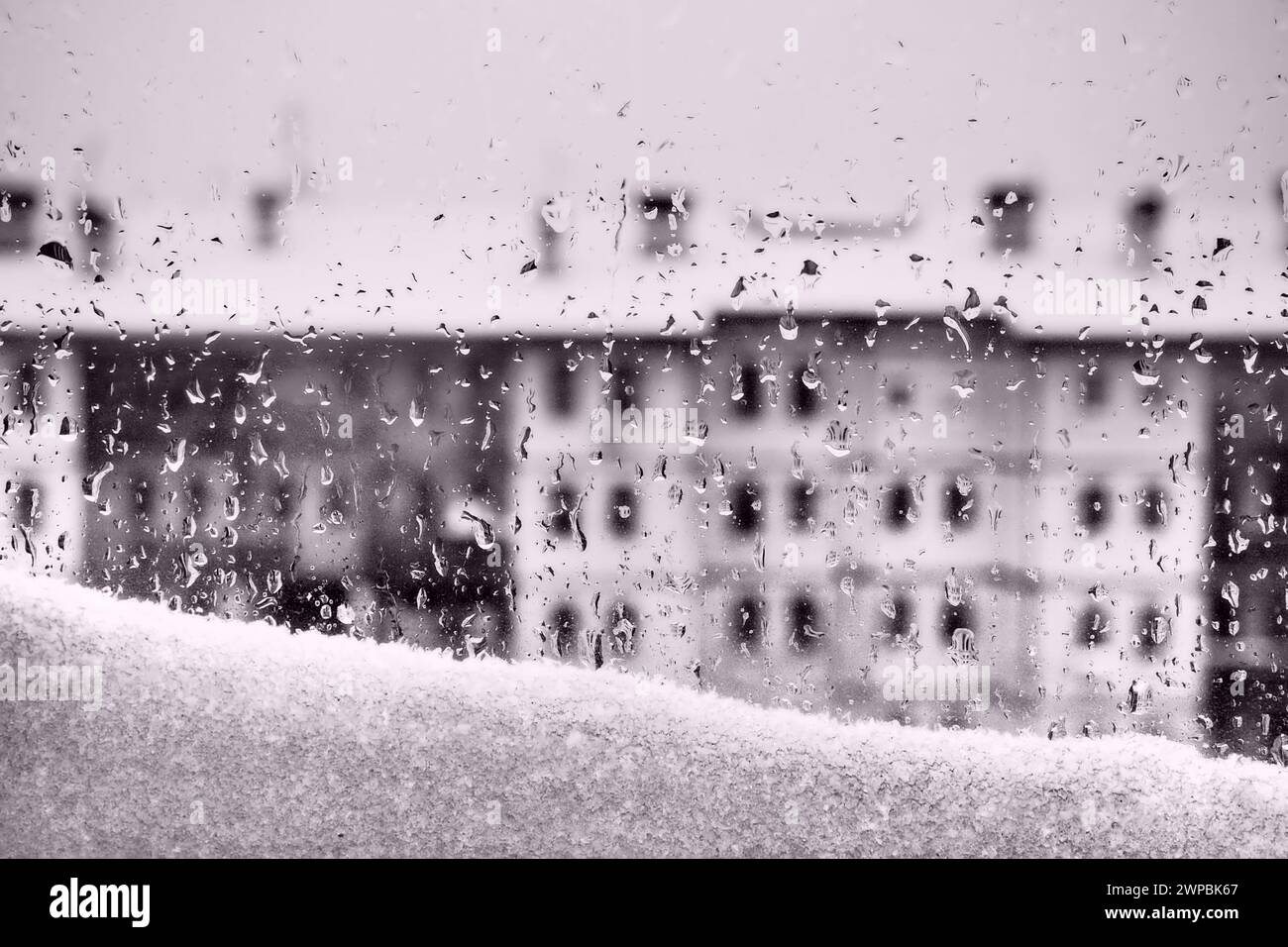 View from the window to the winter thaw. Melting snowdrift and drops on the glass. Multi-storey building with many windows. Christmas New Year Stock Photo