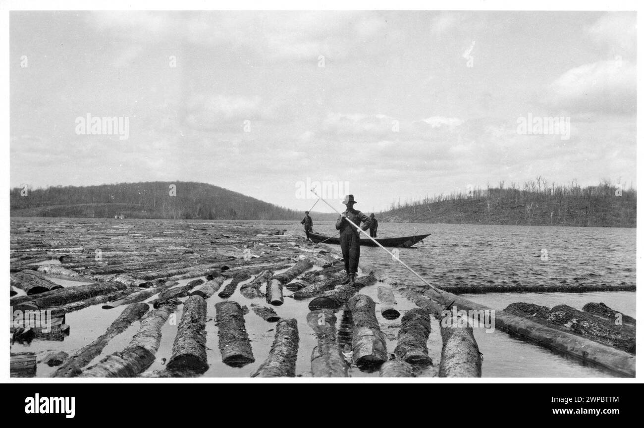 Vintage Historical Photograph. Log driving Yellow birch log boom.  Loogers riding logs down the river to bring cuts to sawmill   Ontario, Canada. 1915 Stock Photo