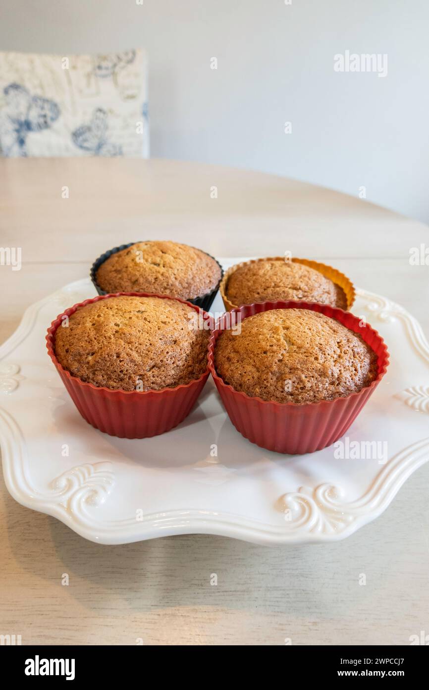 Four homemade fresh-baked banana nut muffins in silicone cups on a white plate. USA. Stock Photo