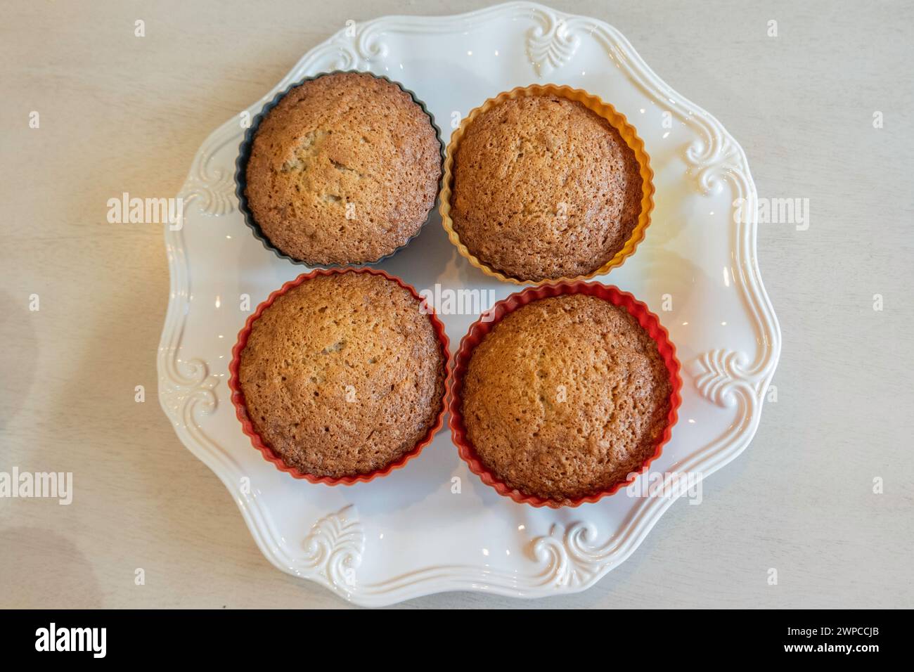 Four home made fresh-baked banana nut muffins in silicone cups on a white plate. Shot from above. USA. Stock Photo