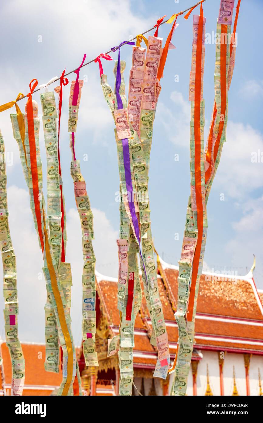Thai banknotes attached to a rope flutter in the wind in a Buddhist temple area Stock Photo
