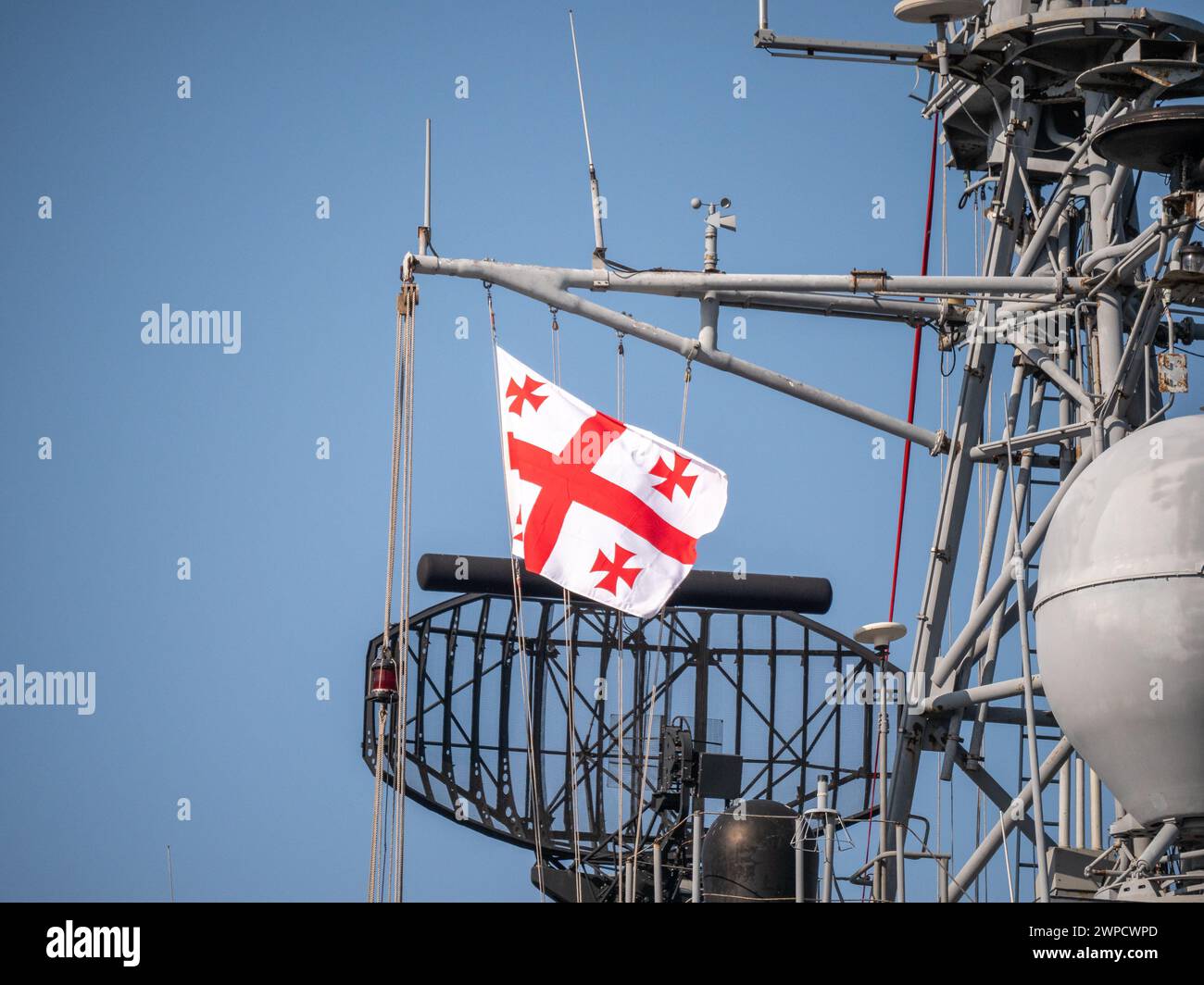 Georgian flag fluttering on naval ship radar tower, with intricate communication equipment against blue sky Stock Photo
