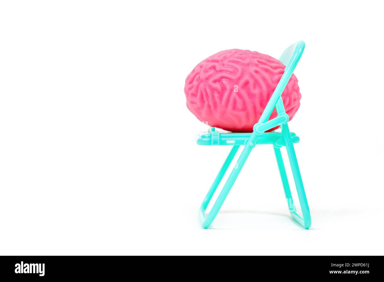 Soft human brain model comfortably seated on a folding teal chair isolated on white background with copy space. Creative medical check-up concept. Stock Photo