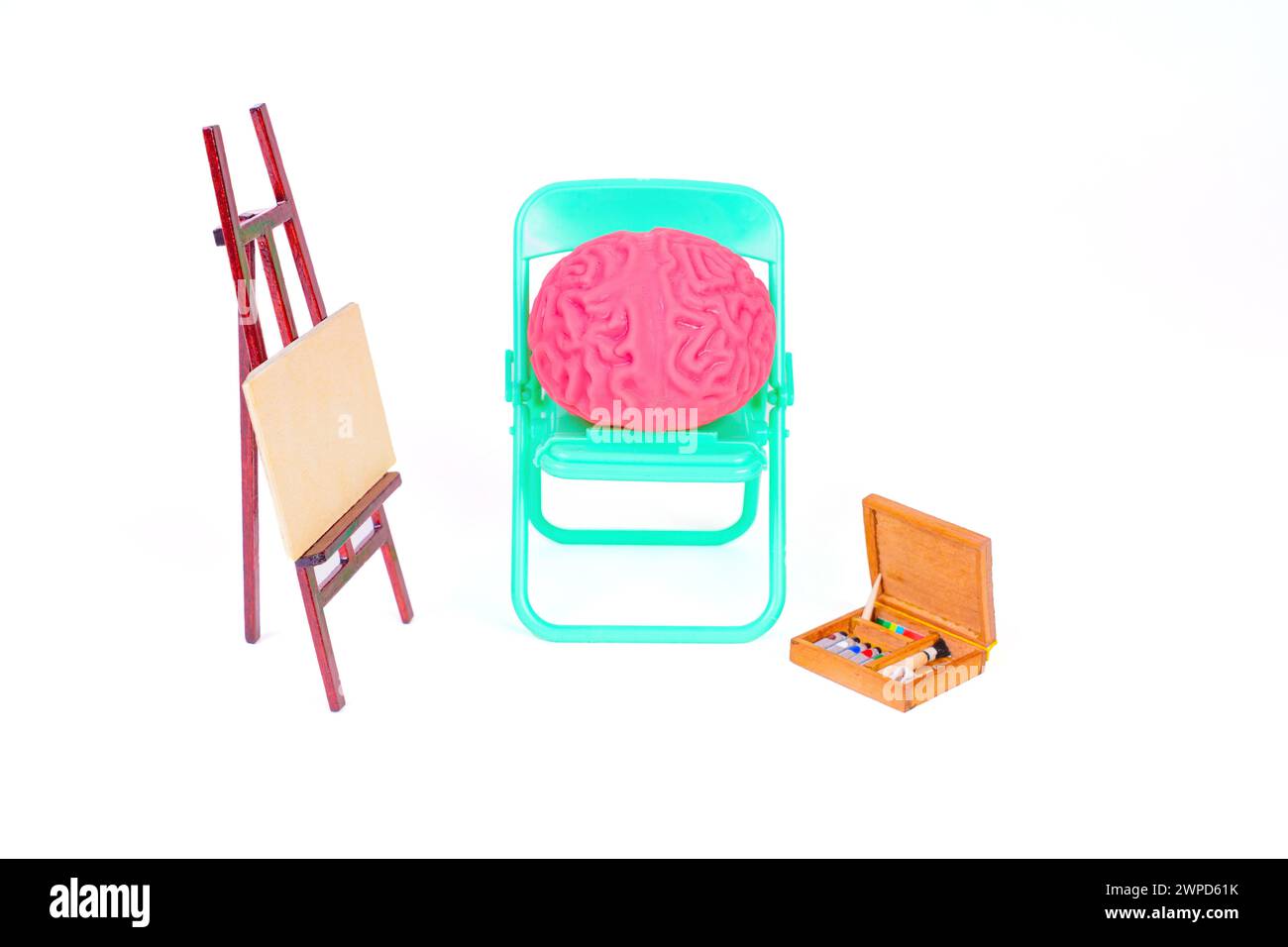 Soft pink brain model seats on a folding chair by an easel and a wooden box of paints. AI and modern digital art concept. Stock Photo