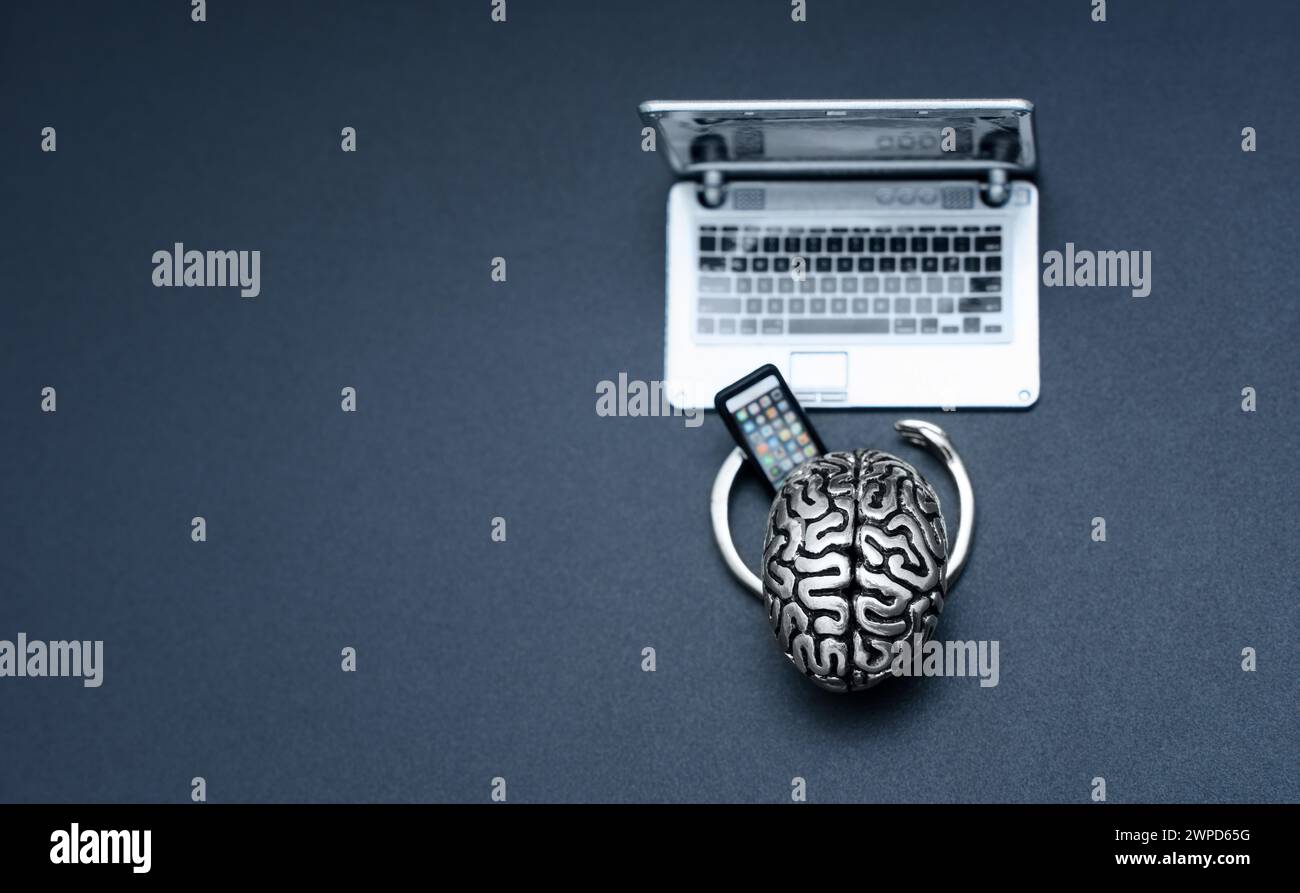 Steel brain with small hands, skillfully holding a mobile phone while working at a laptop isolated on black background with copy space. Artificial int Stock Photo