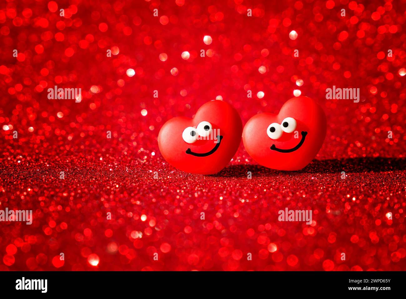 Two joyous heart characters adorned with smiles set against a backdrop of sparkling red. Valentine's Day card full of romance and bliss. Stock Photo
