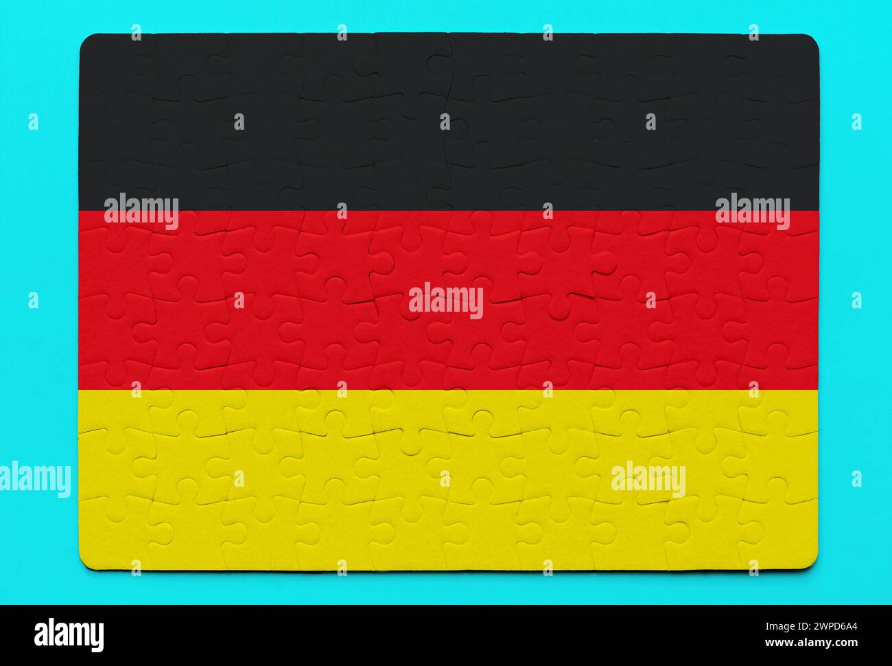 Assembled German flag jigsaw puzzle rests on a vibrant blue background. Unity, nationalism and problem-solving related concept. Stock Photo