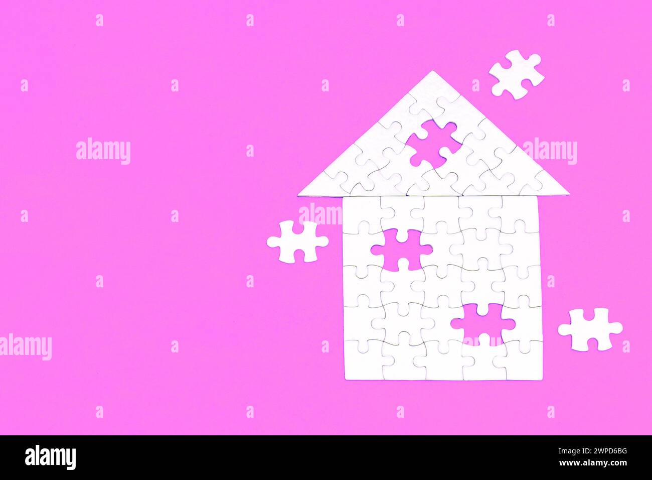 Hip roof house shape crafted from white puzzle pieces set on pink backdrop. Three final elements awaiting their place. Building a dream house. Stock Photo