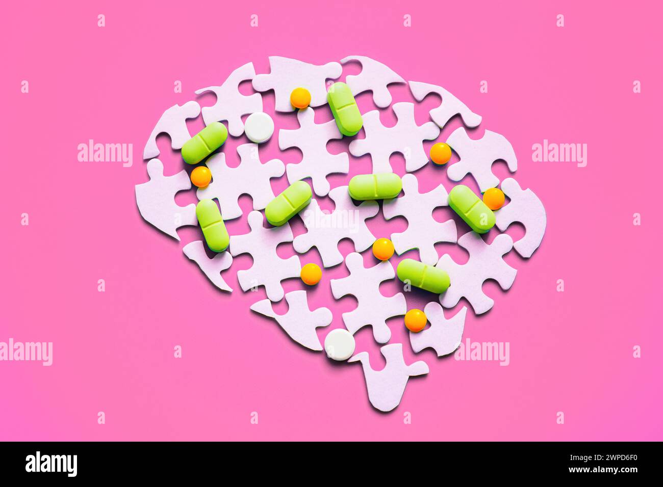 Colorful pills scattered on a disassembled brain puzzle isolated on pink backdrop. Mental health and medication concept. Stock Photo