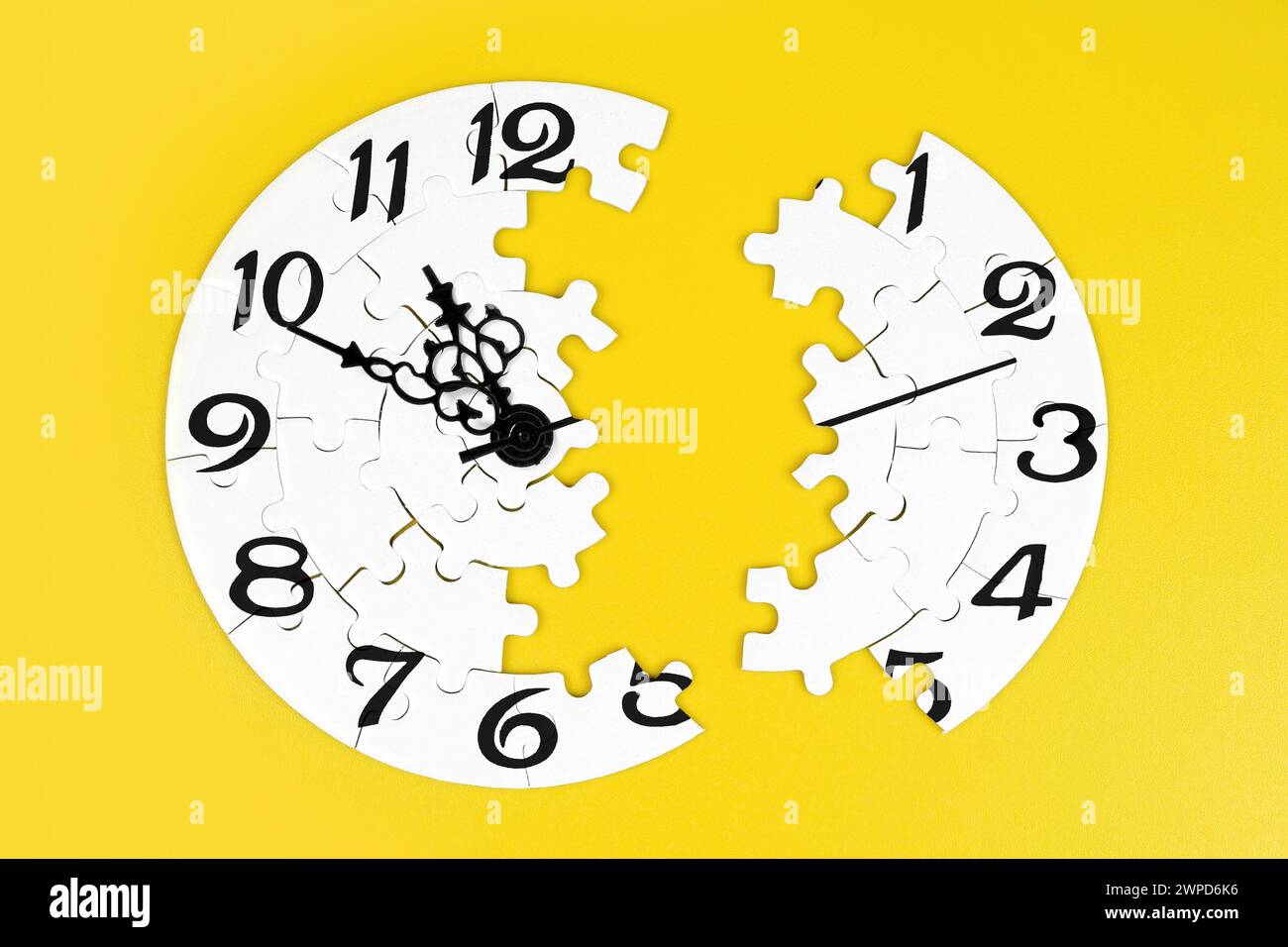 Close-up capture of a clock puzzle split unevenly in two sections, set against a yellow backdrop. Creative business and time-related concept. Stock Photo