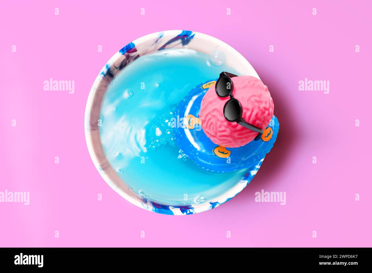 Makeshift oasis inside a cup, where a pink brain, sporting sunglasses, relaxes on an inflatable ring. Creativity, leisure and imaginative escape conce Stock Photo