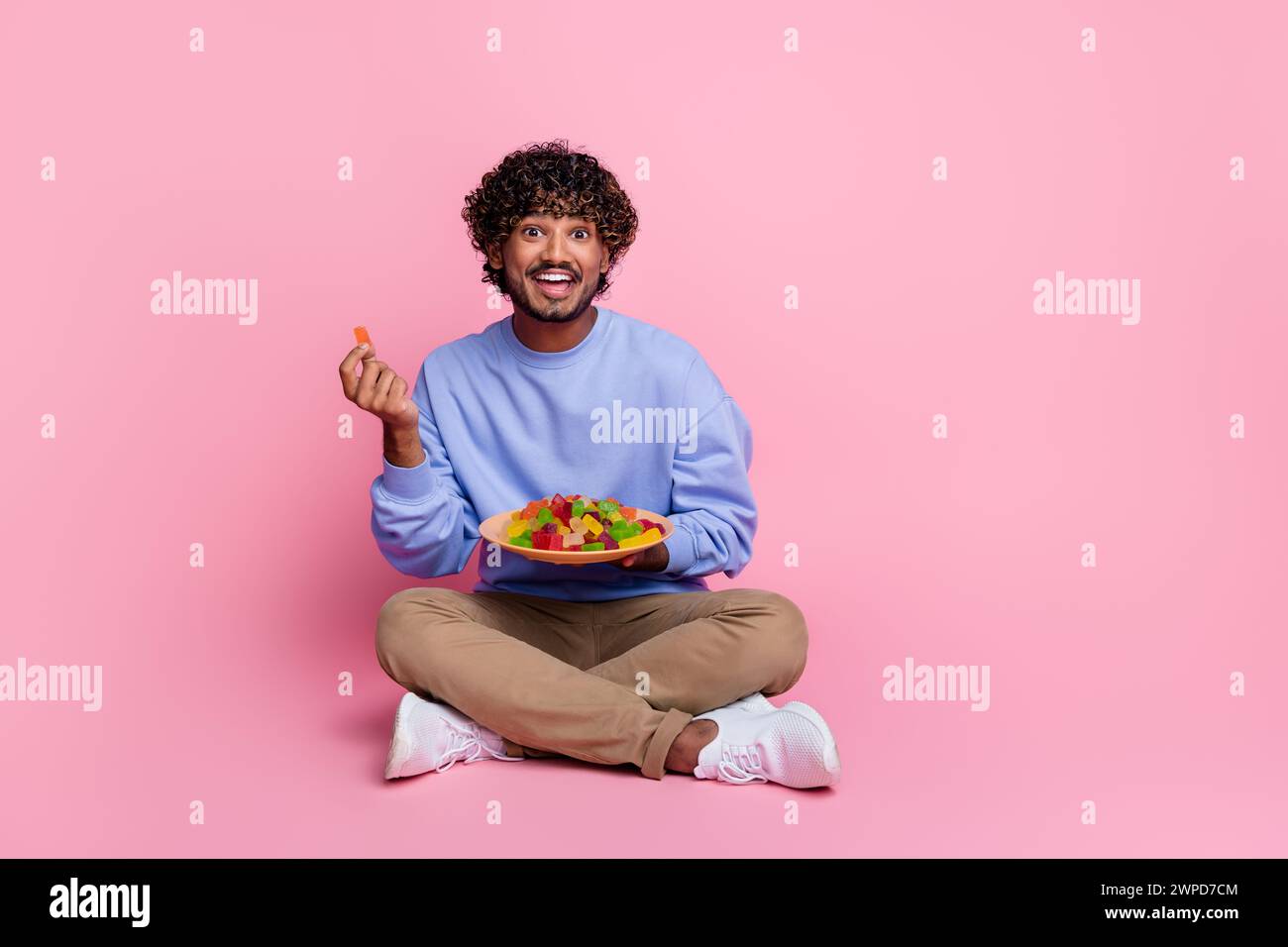 Photo of cheerful funny guy sitting enjoying delicious candies snack ...