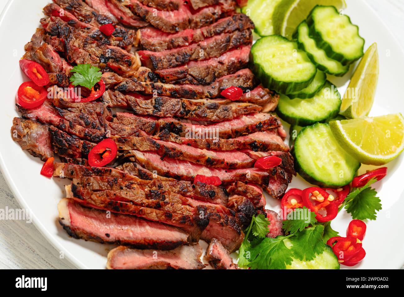 crying tiger, grilled and thinly sliced ribeye steak with cucumber and lime on plate on white