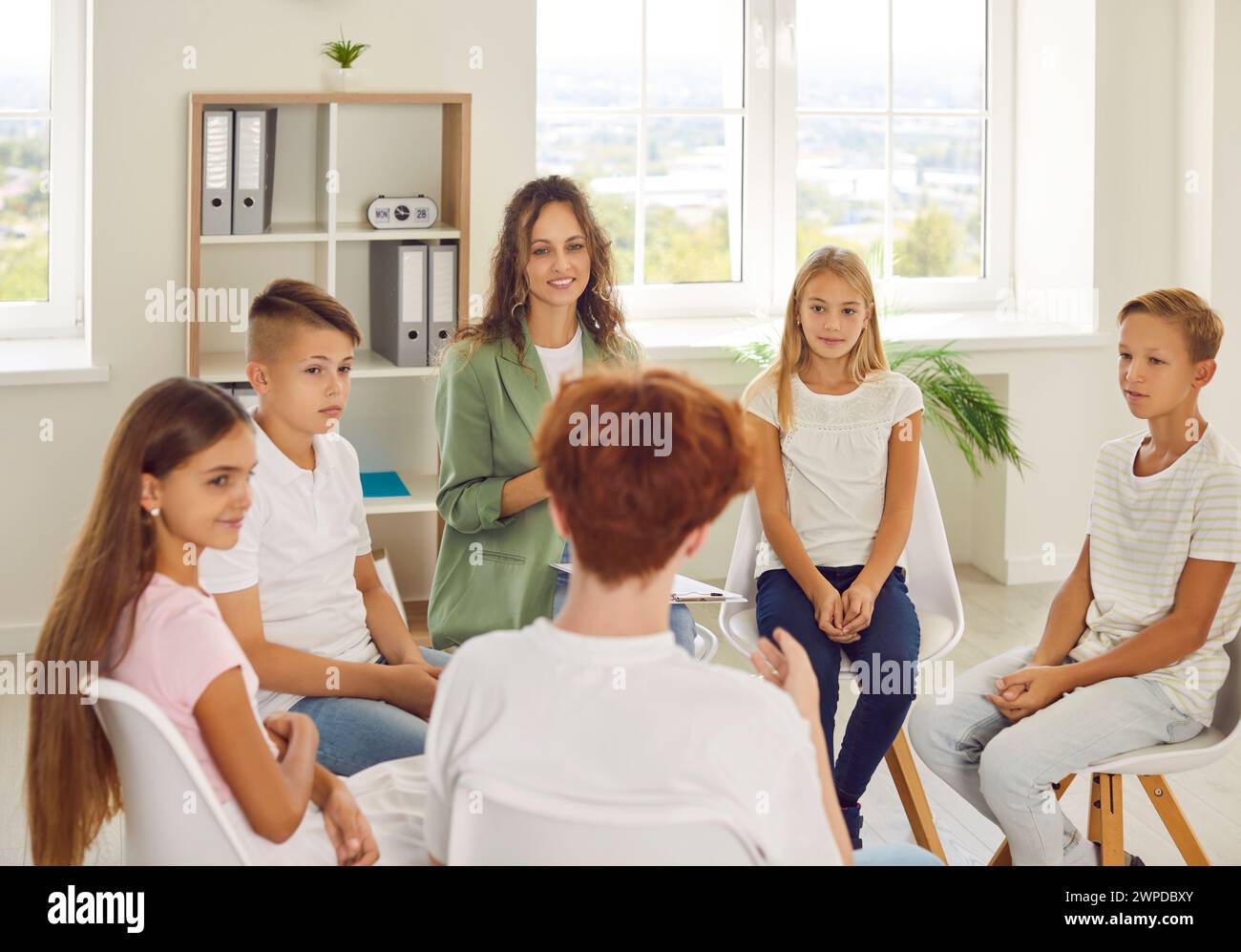 Friendly counselor is talking to group of junior high school students at psychological session. Stock Photo