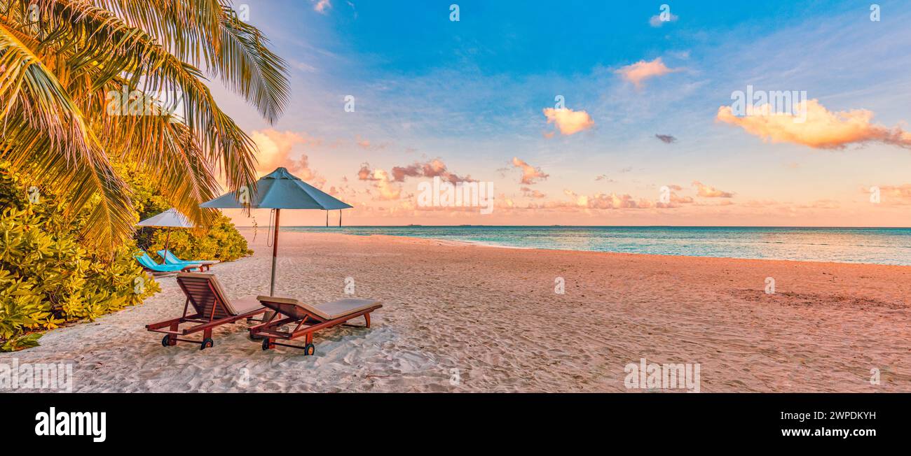 Amazing sunset beach. Romantic couple chairs umbrella. Tranquil togetherness love concept scenery, relax beach, beautiful landscape panorama. Getaway Stock Photo