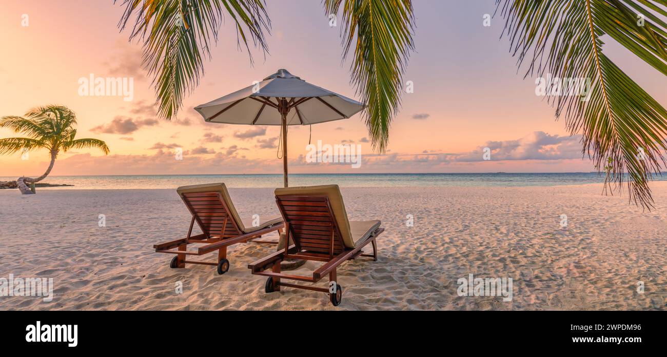 Amazing sunset beach. Romantic couple chairs umbrella. Tranquil togetherness love concept scenery, relax beach, beautiful landscape panorama. Getaway Stock Photo
