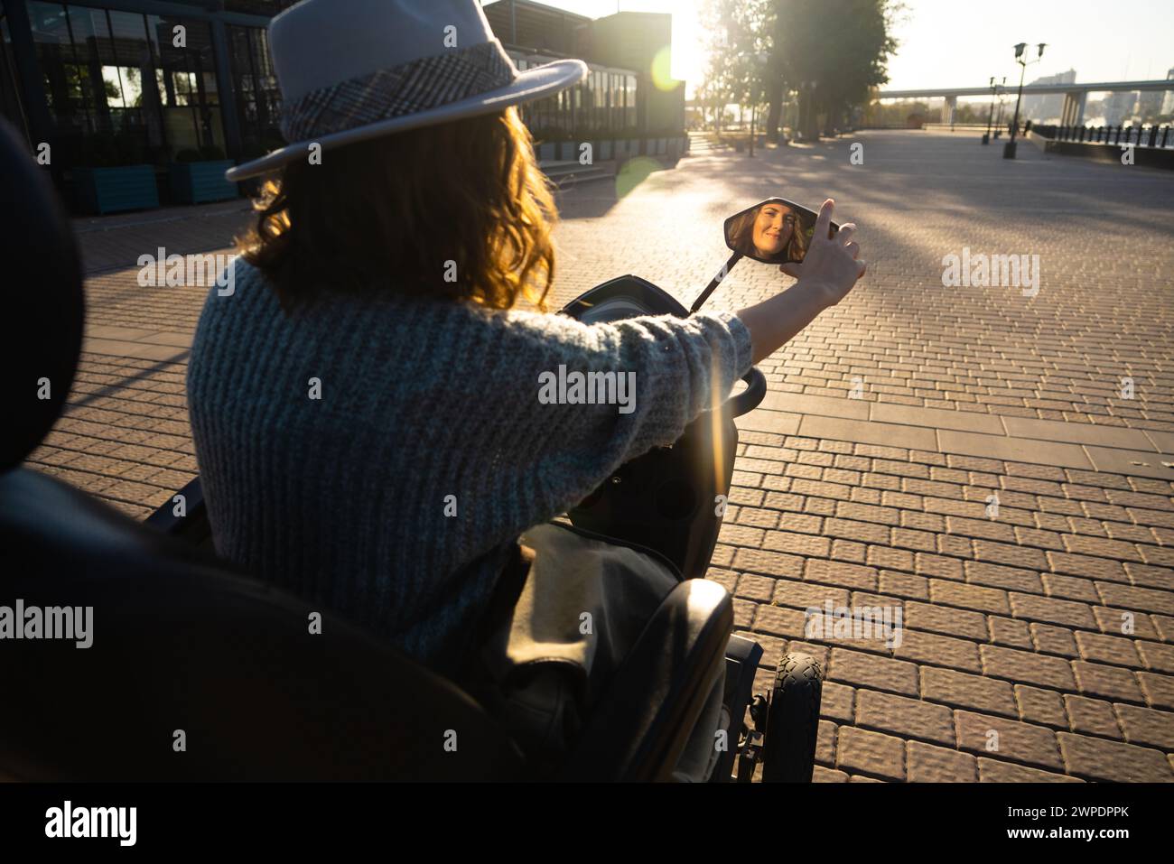 Woman tourist on a four wheel mobility electric scooter on a city street. The woman's face is visible in the rearview mirror. Stock Photo