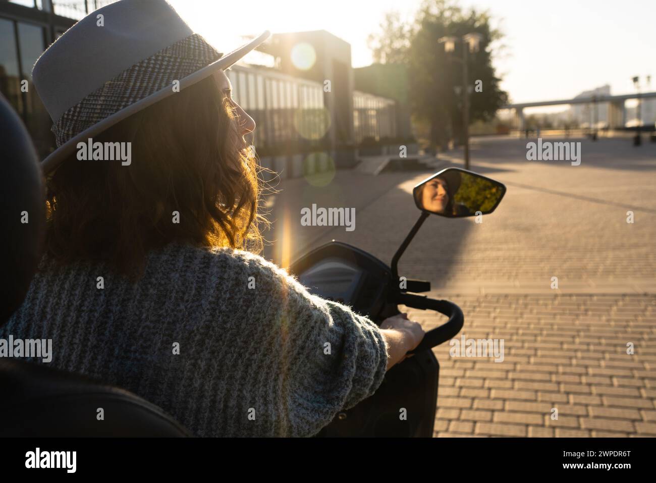 Woman tourist on a four wheel mobility electric scooter on a city street. The woman's face is visible in the rearview mirror. Stock Photo