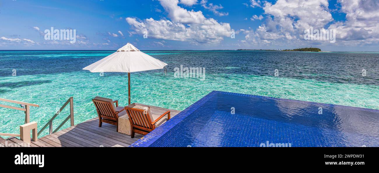 Luxury beach resort, bungalow near endless pool over beautiful blue sea. Amazing tropical island, summer vacation concept. Couple chairs with umbrella Stock Photo