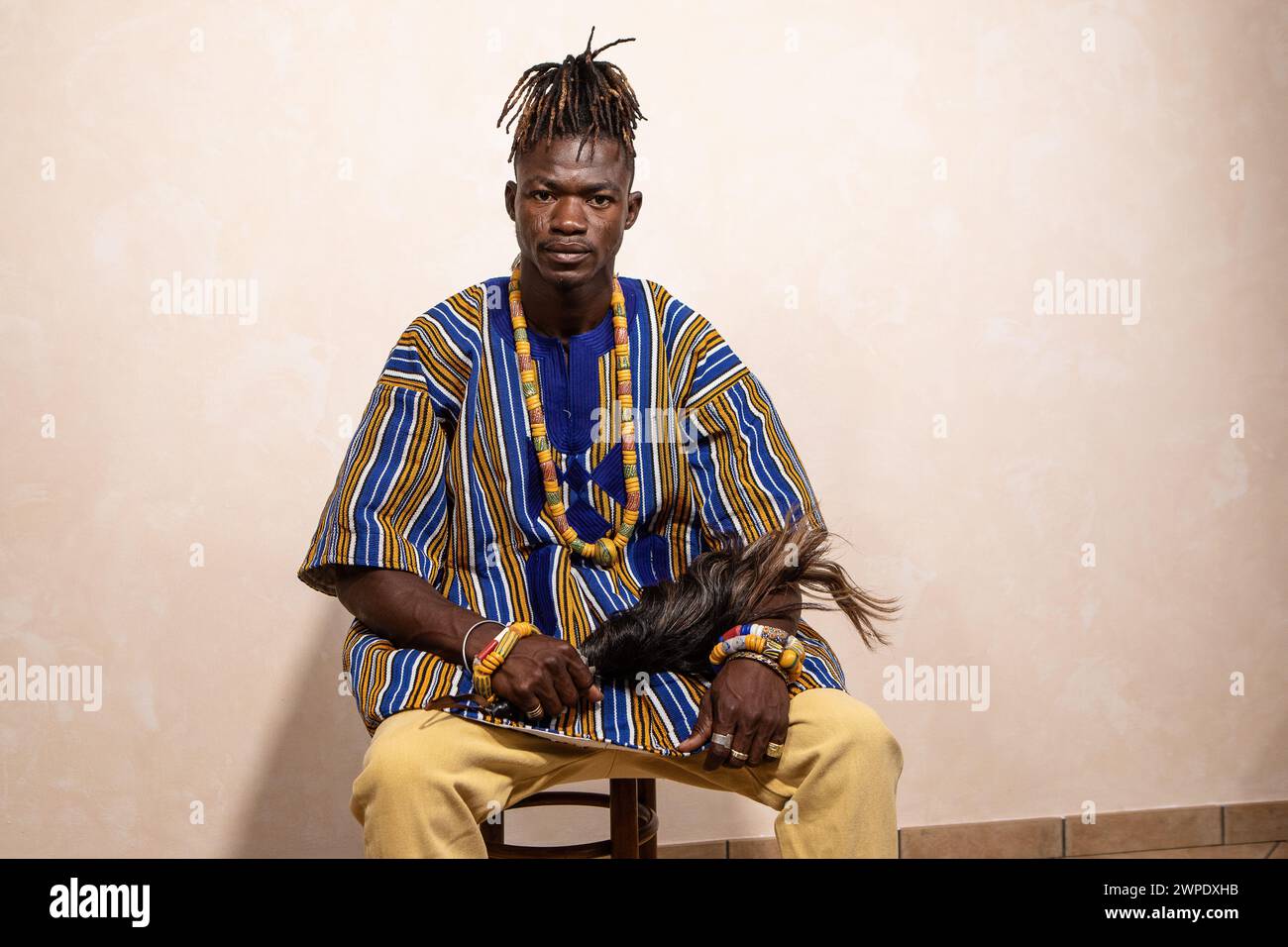 Seated African man in colorful traditional garb, holding a feather ...