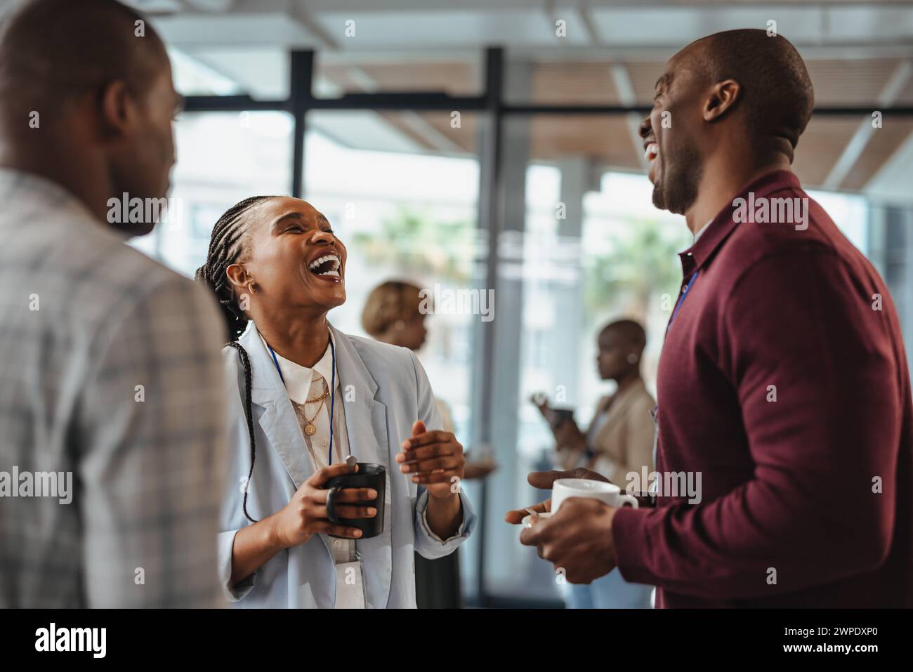 Three business professionals share a laugh during a coffee break at work. Group of colleagues having a funny conversation while standing together in a Stock Photo