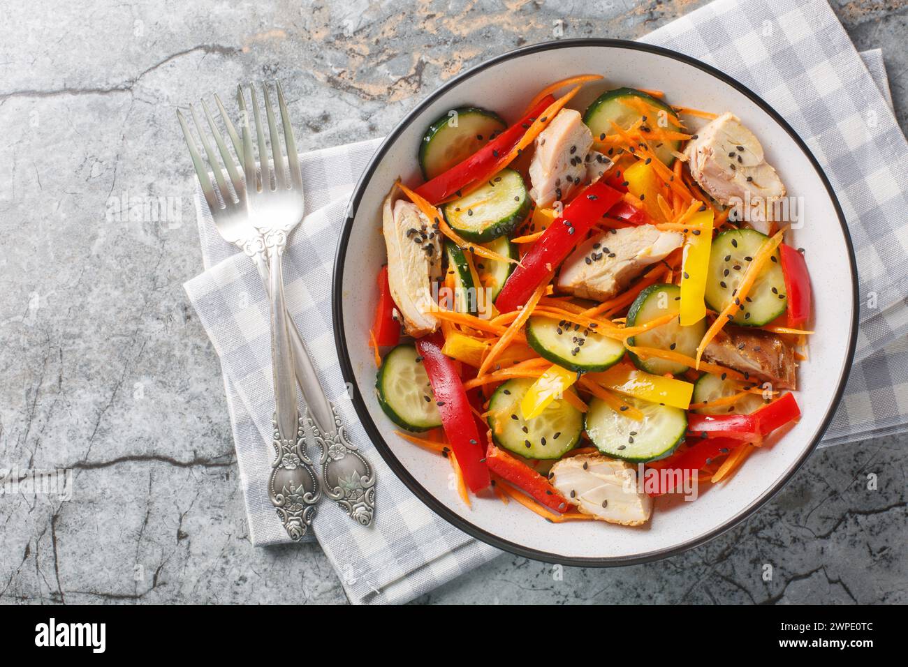Vitamin salad with baked chicken, fresh cucumbers, bell peppers, carrots and sesame seeds close-up in a bowl on a marble table. Horizontal top view fr Stock Photo