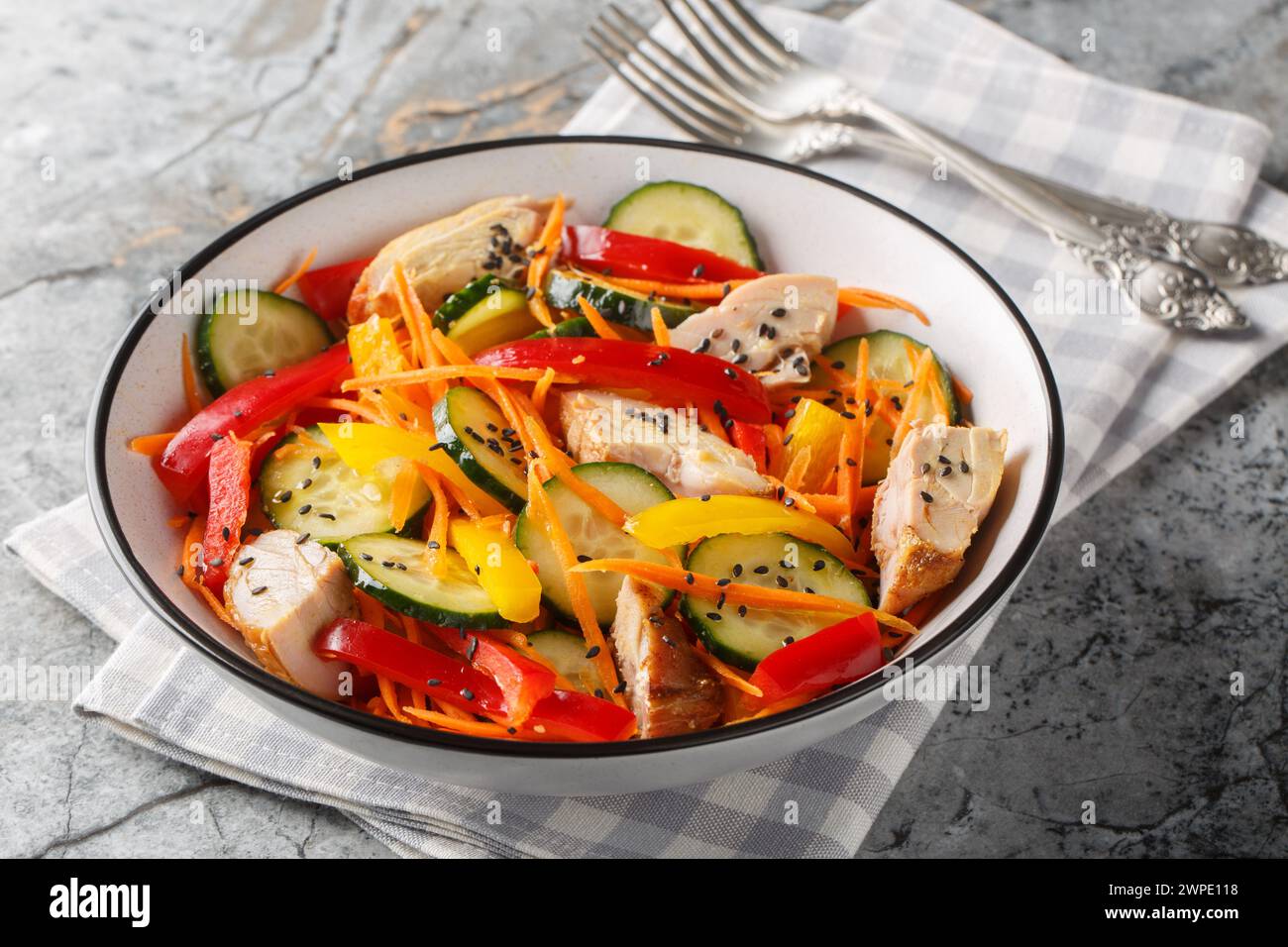 Healthy food Chicken salad with fresh cucumbers, bell peppers, carrots and sesame seeds close-up in a bowl on the table. Horizontal Stock Photo