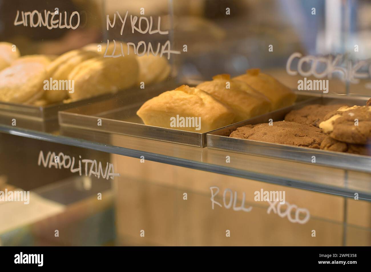 Display case with a variety of cakes and cookies, labeled, in an illuminated pastry shop. Stock Photo