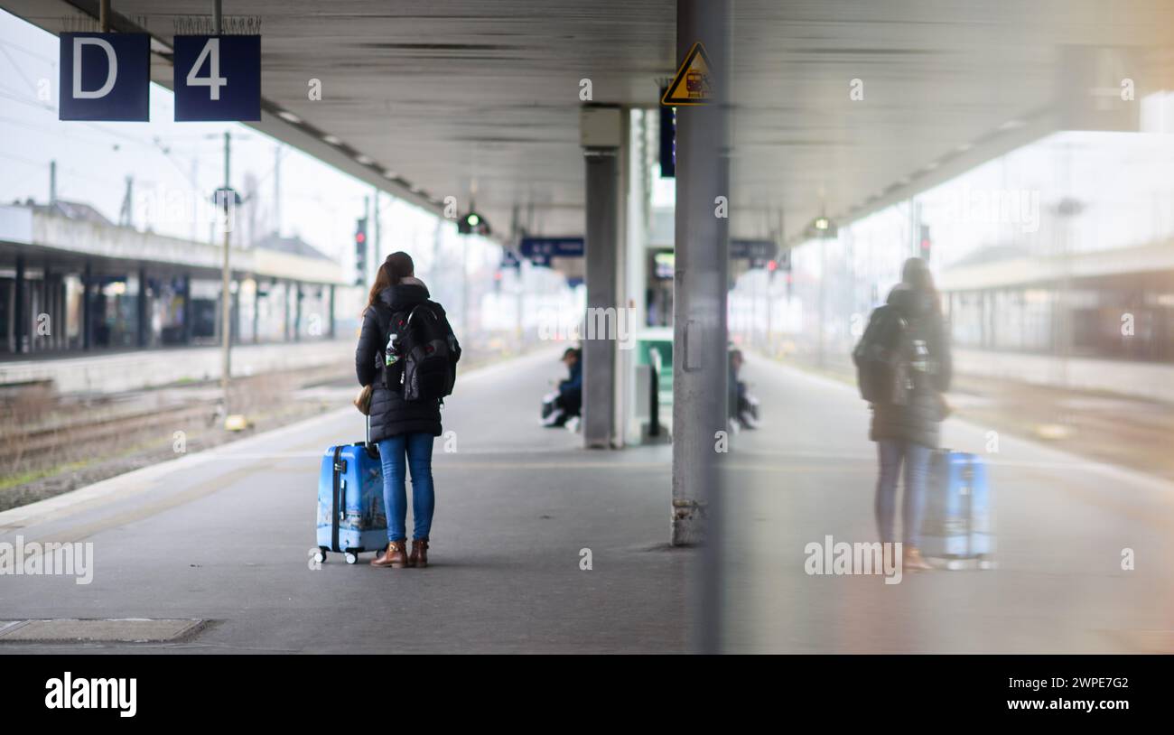 Hanover, Germany. 07th Mar, 2024. A woman waits with a suitcase on platform 4 at Hanover Central Station and is reflected in a pane of glass. In the wage dispute with Deutsche Bahn, the GDL union has called for 35-hour strikes in both passenger and freight transport. Credit: Julian Stratenschulte/dpa/Alamy Live News Stock Photo