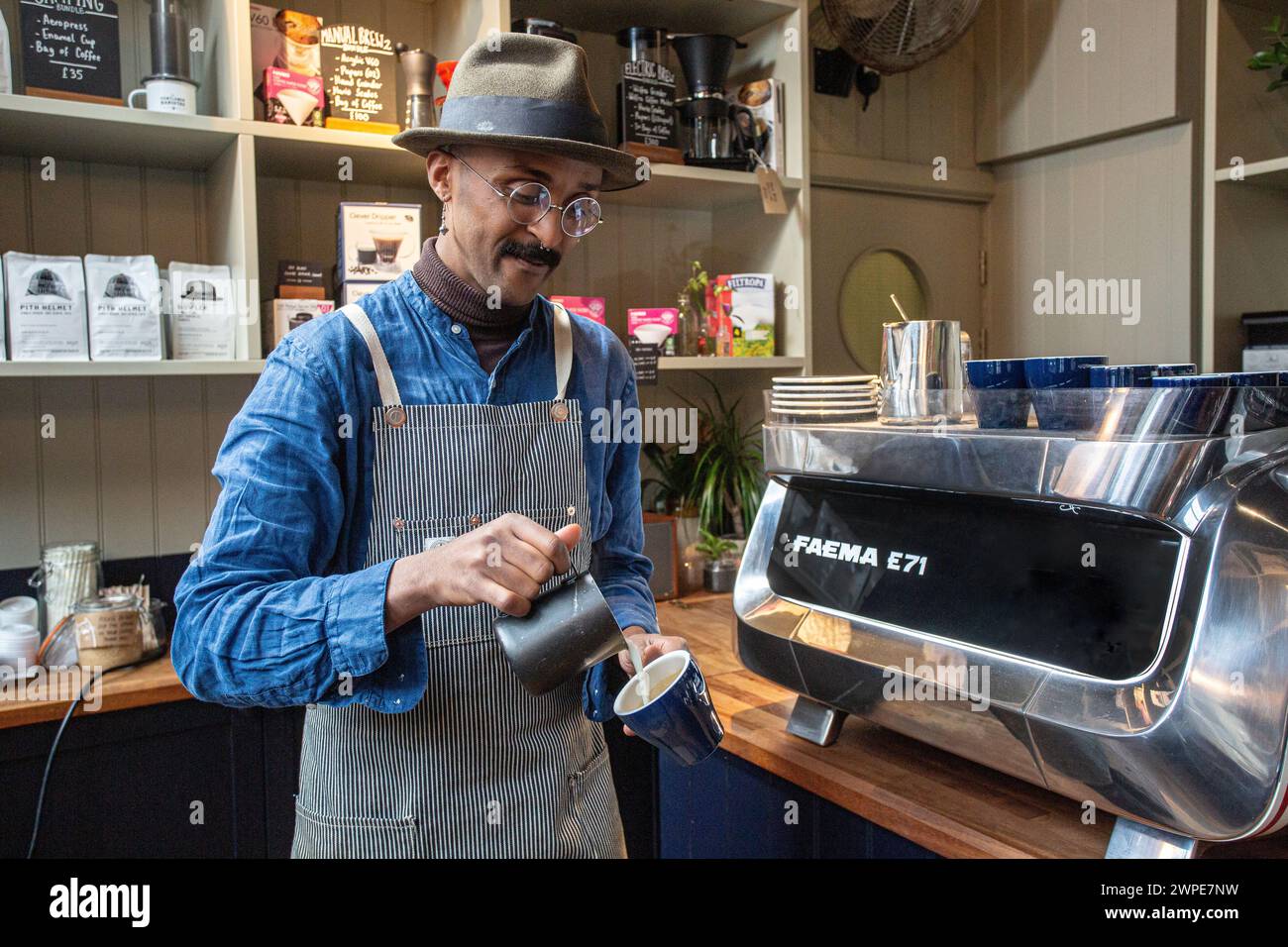 barista with apron pouring steamed milk into coffee cup making a flat white Stock Photo