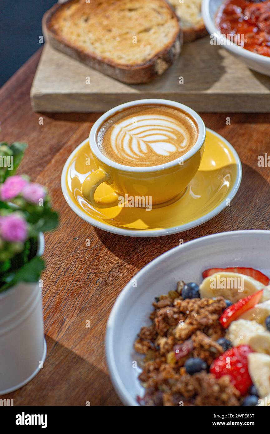 A cup of flat white, toast and bowl of granola on table in caffee. Stock Photo