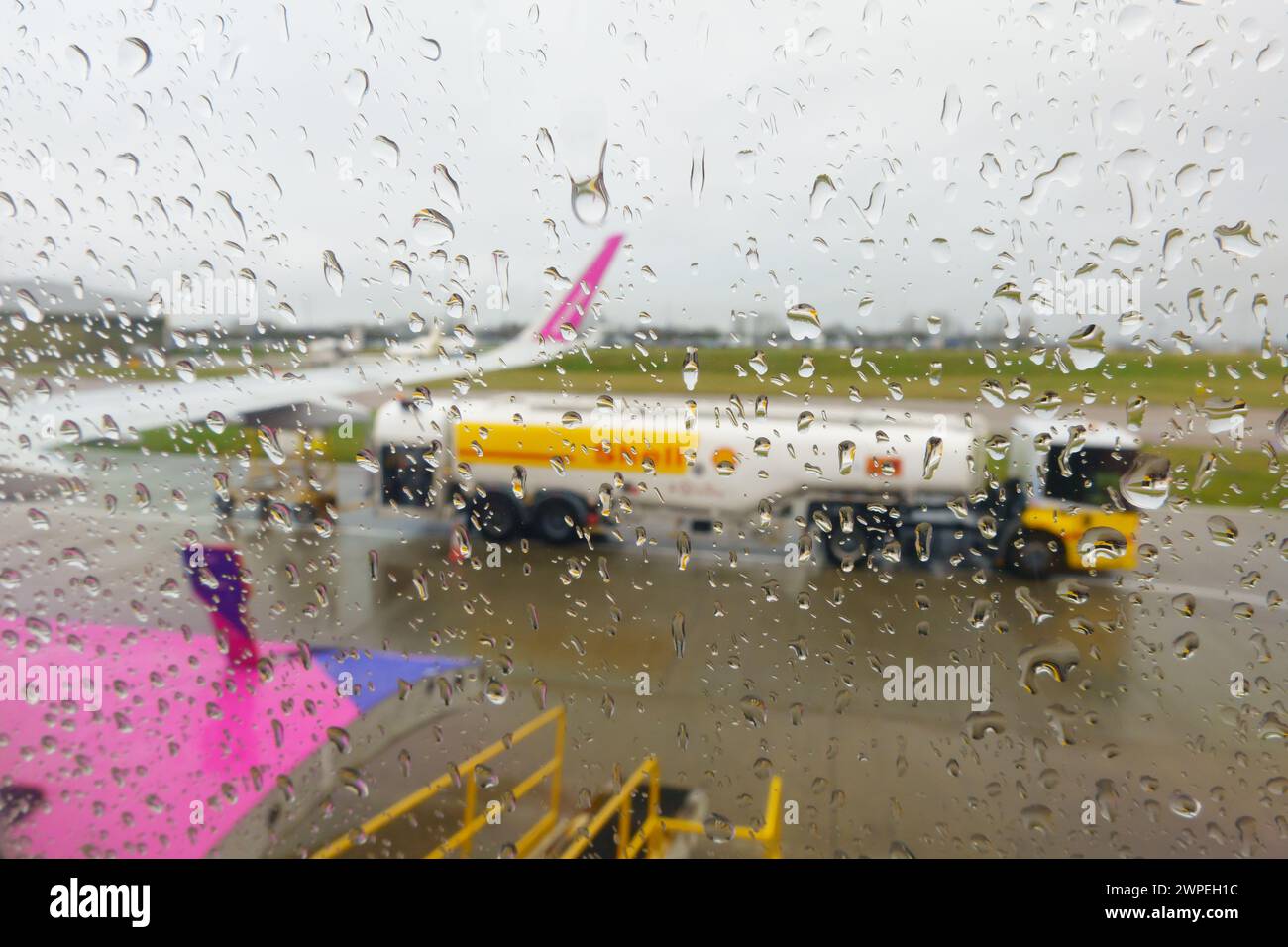 Rainy day raindrops on an airliner window, diffusing the aviation fuel tanker and aircraft wing, on the apron at London Luton Airport. Stock Photo