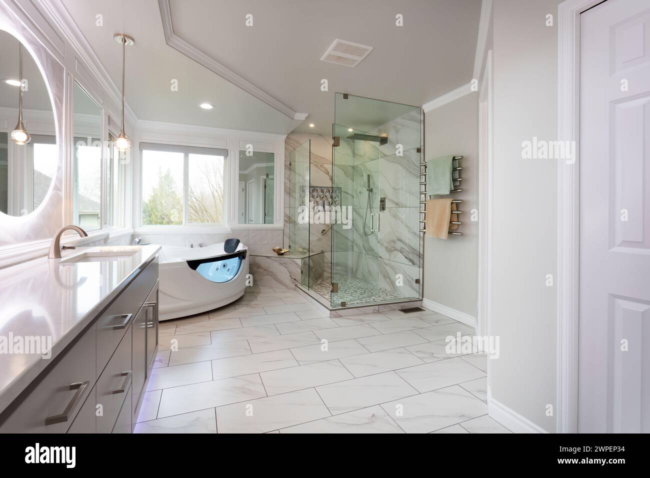 Spacious modern contemporary master bathroom with jacuzzi hot tube, large glass walk in shower, new stone counter, wall, mirrors, lighting plus towel Stock Photo