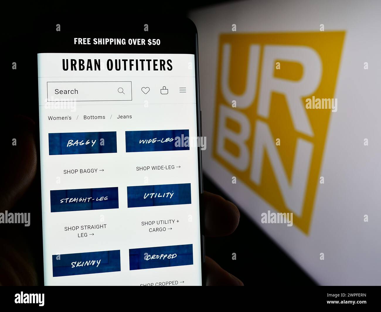Person holding smartphone with webpage of US fast-fashion company Urban Outfitters Inc. (URBN) in front of logo. Focus on center of phone display. Stock Photo
