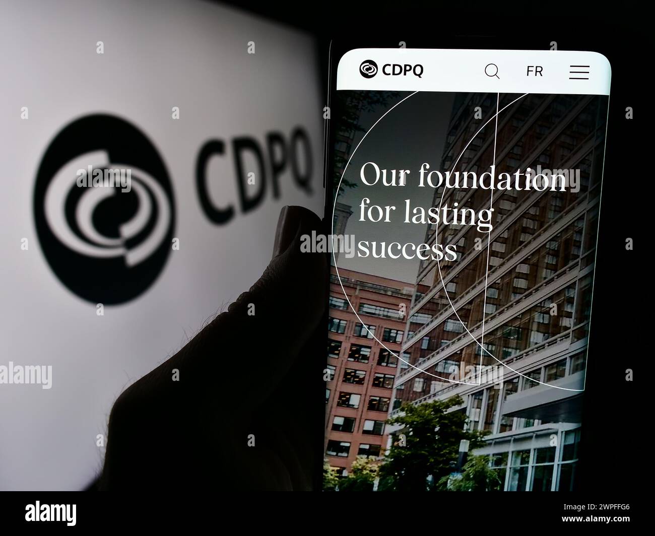 Person holding cellphone with webpage of Caisse de Depot et Placement du Quebec (CDPQ) in front of logo. Focus on center of phone display. Stock Photo