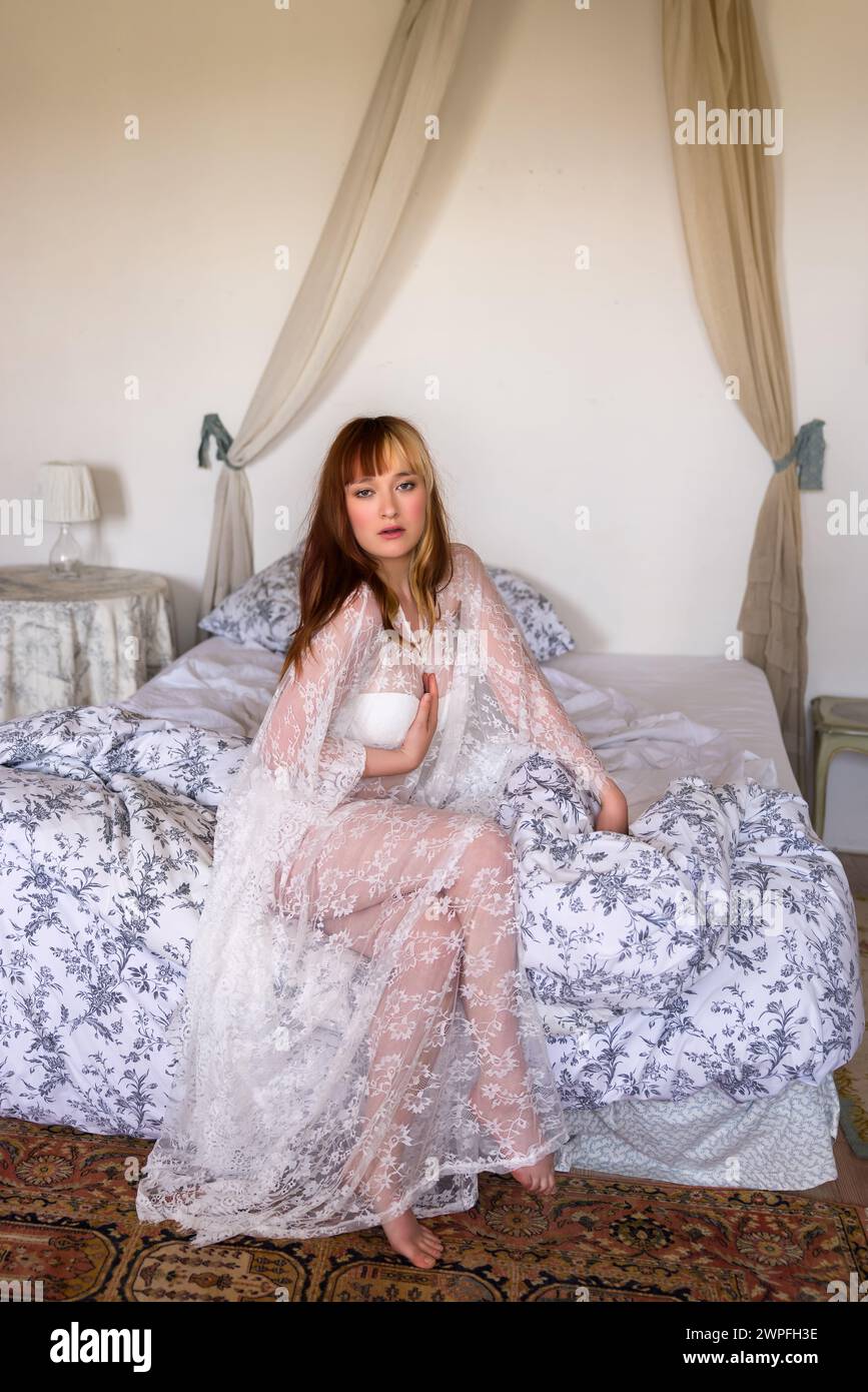 Woman in lace nightgown sitting on canopy bed Stock Photo