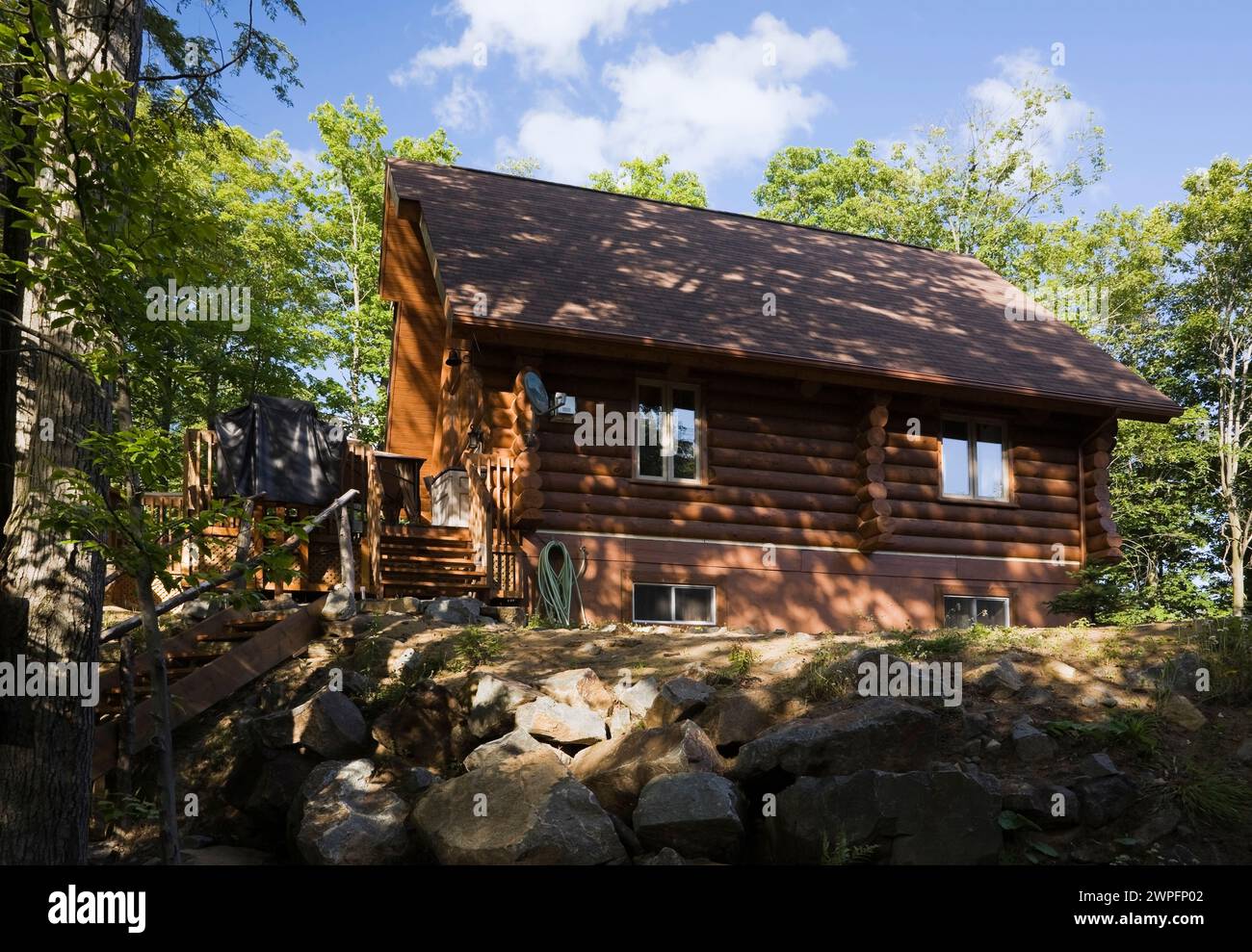 Milled log home with brown asphalt shingles roof in summer. Stock Photo