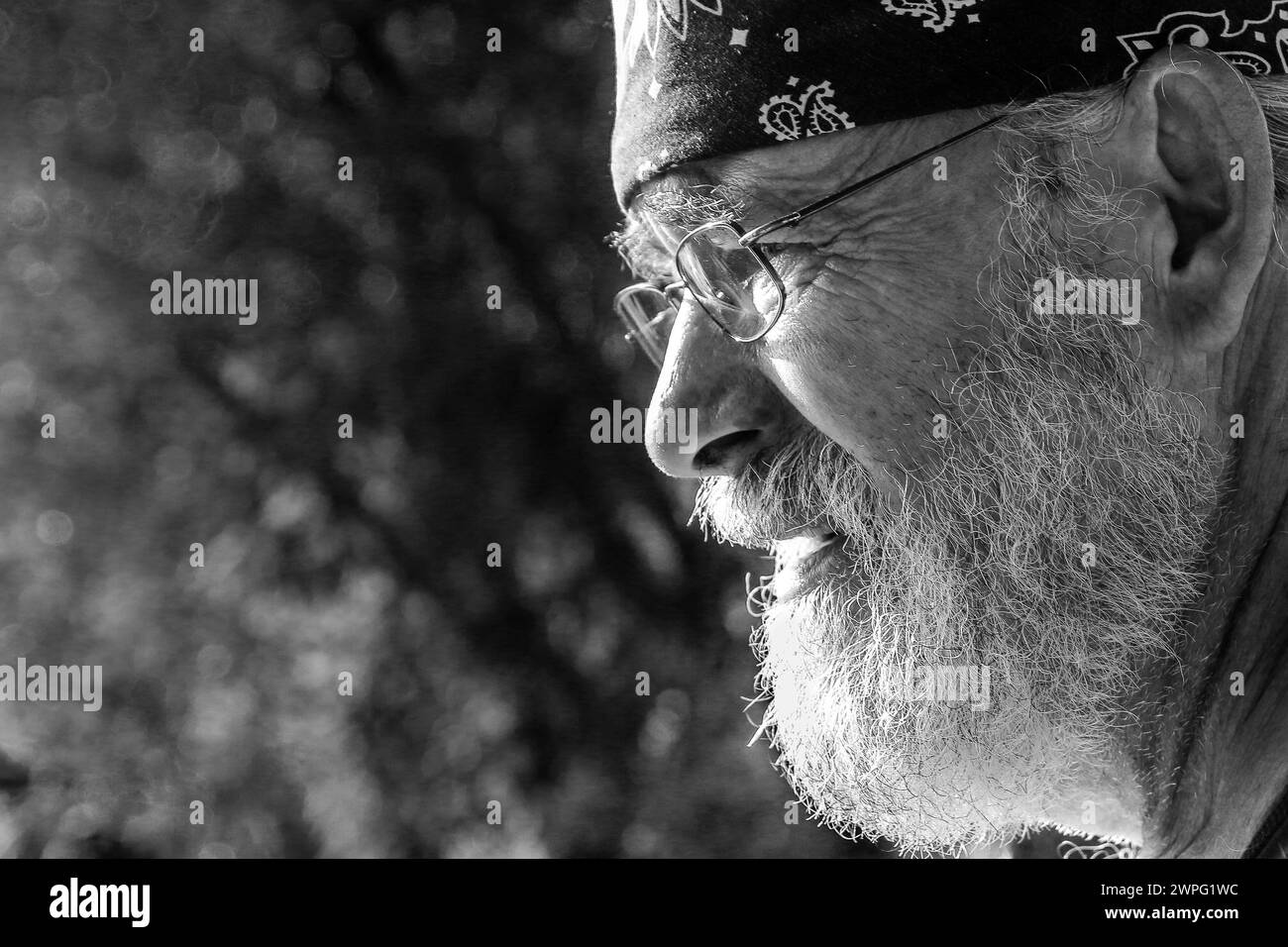 Close-up of old Hippie man wearing a bandana and glasses with a gray beard deep in thought, thinking memories perhaps with regret or worry. Stock Photo
