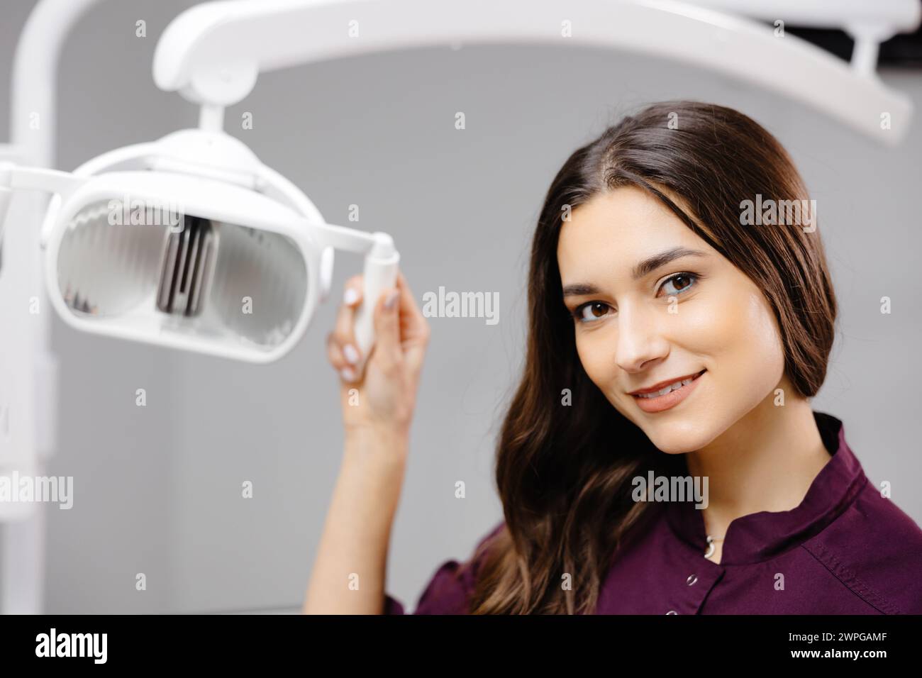 Caucasian female dentist turning on lamp before treatment, smiling to male patient. Stock Photo