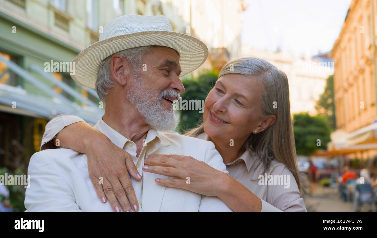 Portrait joyful aged Caucasian happy family elderly wide smiling pensioners woman hugging embrace man looking at camera happiness outdoors city Stock Photo