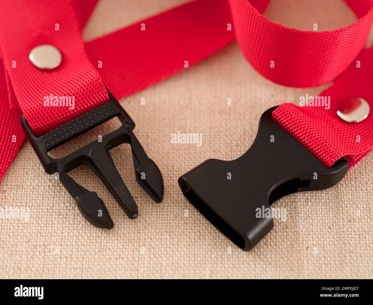 Two ends of a black contoured side release plastic buckle with red nylon belt on a beige textile background Stock Photo