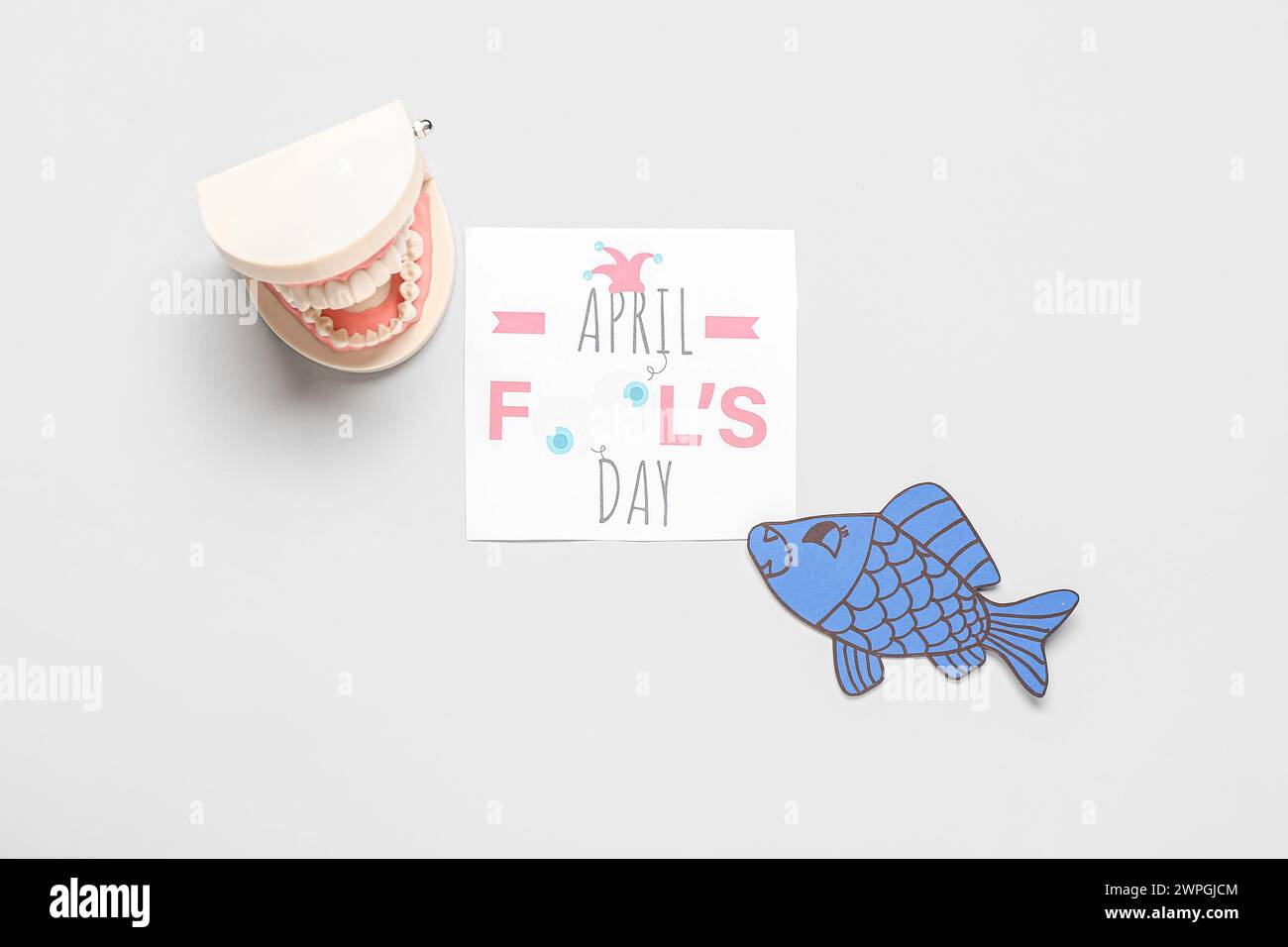 Sheet with text APRIL FOOL'S DAY, model of jaw and paper fish on white ...