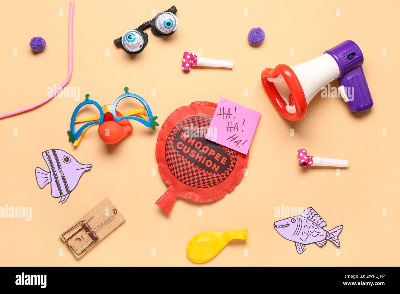 Megaphone with funny glasses, mousetrap and whoopee cushion on beige background. April Fool Day Stock Photo