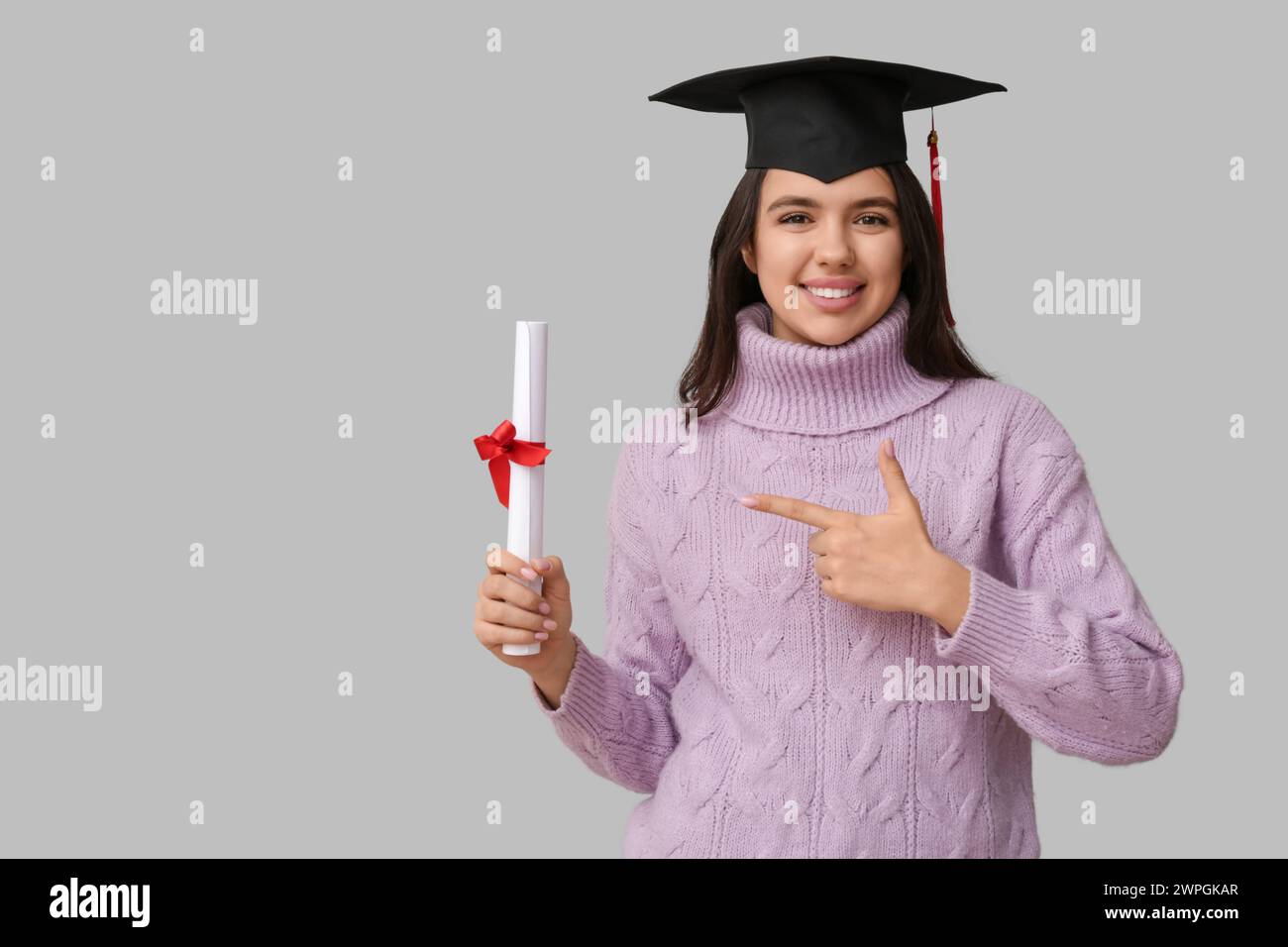 Happy smiling female student in graduation hat pointing at diploma on ...